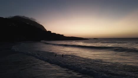 una pareja jugando con grandes olas en el mar sobre las arenas blancas de la playa sudafricana a la hora de la puesta del sol - toma aérea