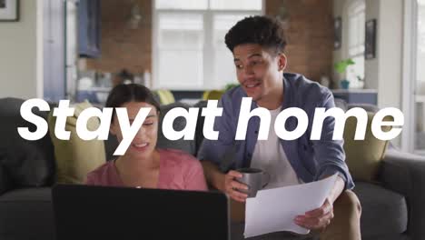 animation of stay at home text over diverse couple using laptop