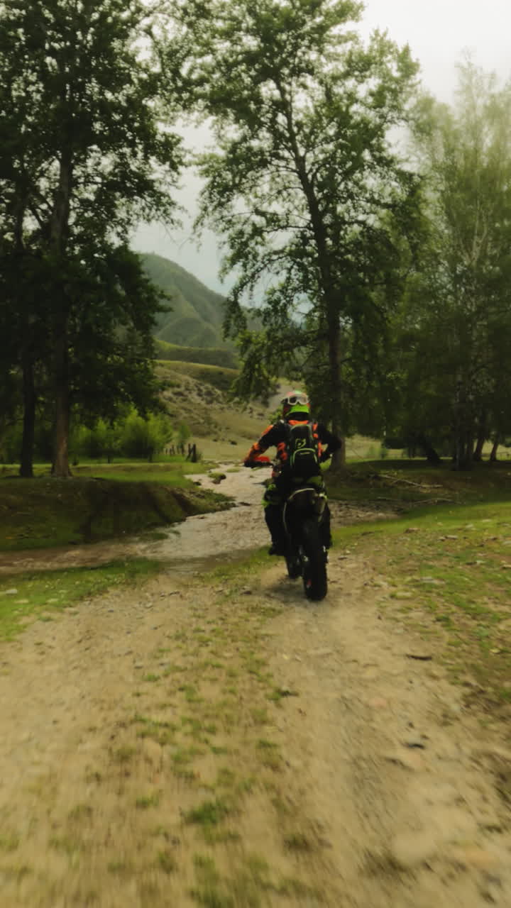 Motorcyclist rides across creek at racing fpv. Courageous biker on motorcycle walkthrough offroad route in virgin nature. Mud drops on camera