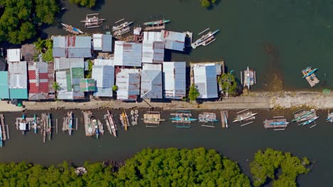 Una-Toma-Aérea-De-Un-Dron-Mirando-Directamente-Hacia-Los-Techos-De-Hojalata-De-Las-Cabañas-De-Pesca-Y-Los-Pequeños-Barcos-De-Pesca-Estilo-Kayak-En-Un-Muelle-De-Concreto