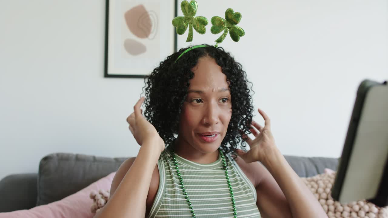 Una donna afroamericana alza le mani e sistema una fascia per capelli a trifoglio, parlando allo schermo.