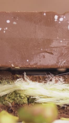 Vertical video of elegant Dubai chocolate enriched with green pistachio crumbles, capturing fine dessert details in sharp macro clarity