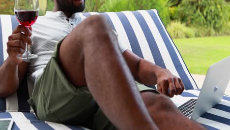 Smiling-man-using-laptop-while-having-wine-in-garden-4k