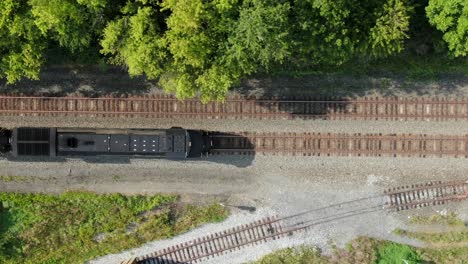 Black diesel locomotive train engine with headlight on, stopped on railroad track, top down overhead aerial drone perspective, switching car, track, freight and travel transportation concept