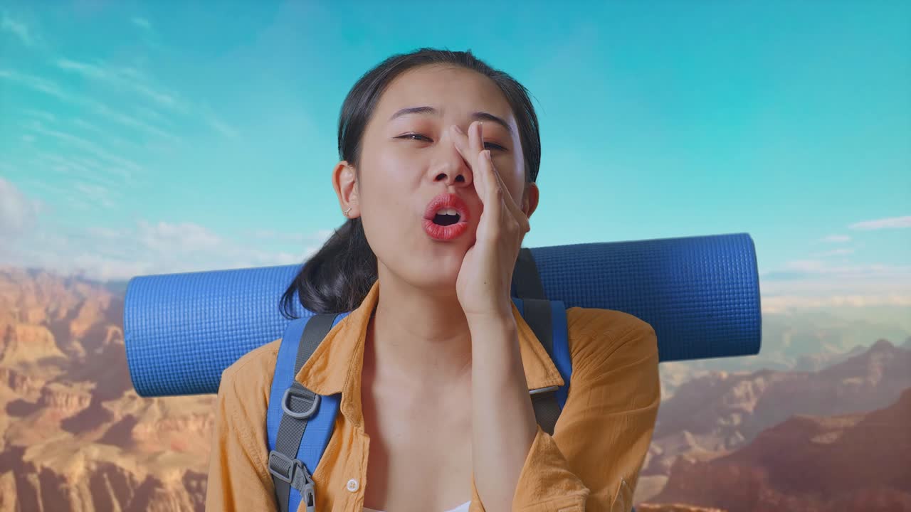 Close Up Of Asian Female Hiker With Mountaineering Backpack Screaming Holding Hands Near Her Mouth While Traveling At The Top Of Mountain