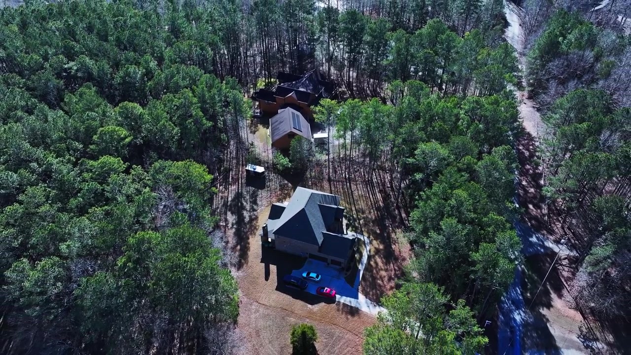 Luksuriøse forstadshuse i Atlanta med mørke tage, solpaneler, indkørsler, parkerede biler omgivet af tæt fyrre- og løvskov under en solrig, klar himmel. Georgia, USA. Luftfoto ovenfra