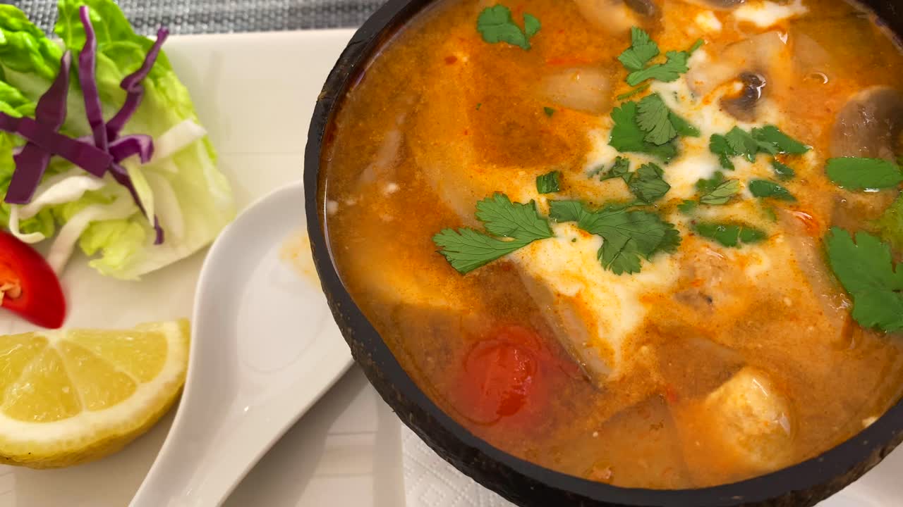 sopa picante tailandesa tom yum con pollo, camarones y verduras en un plato de coco, plato caliente en un restaurante de cocina tailandesa, tiro de 4k