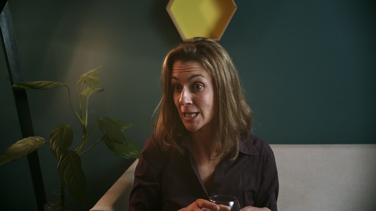 Donna sul divano che sorride e parla con qualcuno con un bicchiere di vino rosso.