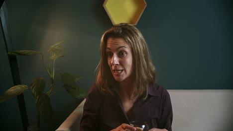 Woman-on-sofa-smiling-and-talking-to-someone-with-a-red-wine-glass