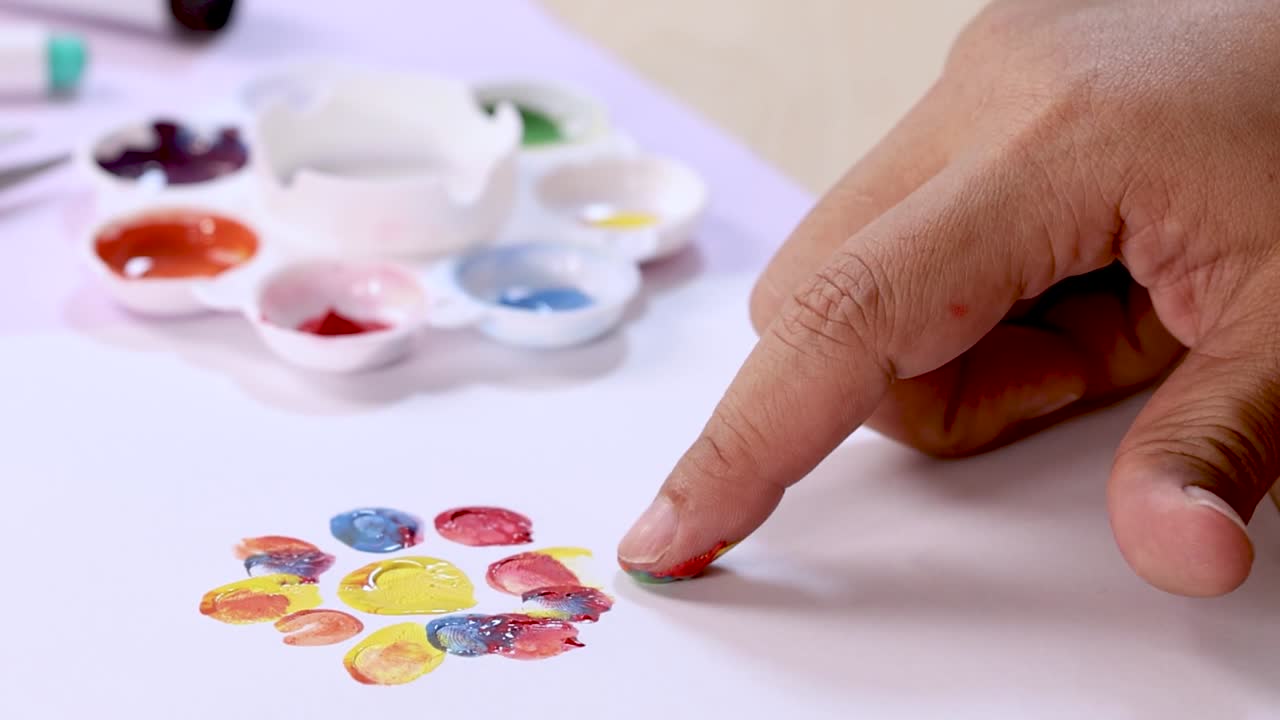 A person uses their fingertip to dab green paint, creating a flower pattern on paper