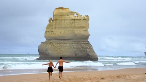 video de cámara de una pareja corriendo en la playa en la parte inferior de los pasos de gibson cerca de los 12 apóstoles a lo largo de la gran carretera del océano en victoria, australia