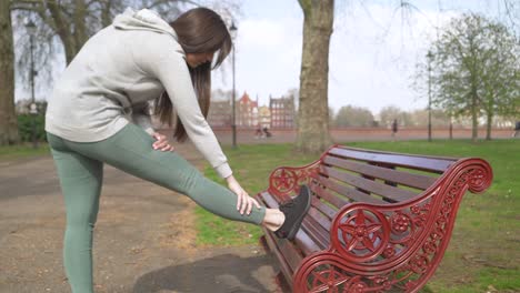 female jogger stretching her leg on a park bench before run