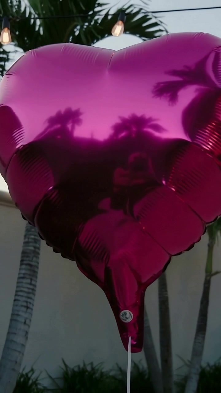 Video verticale: Palloncino magenta che ondeggia, legato in basso su un patio nella brezza, riflettendo le palme.