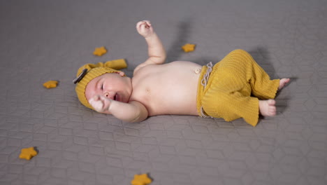 active little boy tossing his feet and hands. funny boy in a yellow costume moving his limbs. grey background.