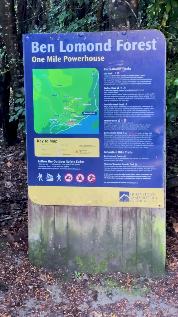A stationary camera captures a clear view of the Ben Lomond Forest trailhead sign surrounded by damp autumn foliage and forest under overcast daylight