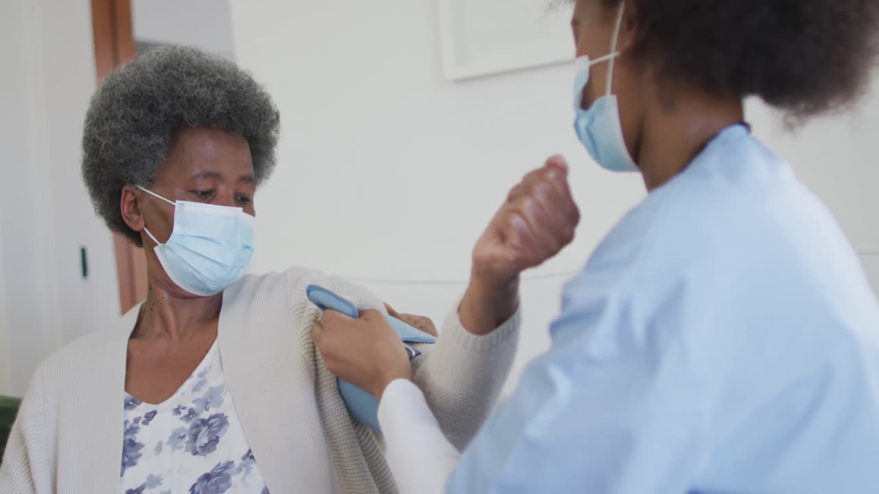 아프리카계 미국인 여성 의사와 고위 여성 환자가 얼굴 마스크를 쓰고 있습니다.