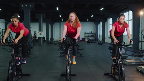 Group-of-girls-performs-aerobic-training-workout-cardio-routine-on-bike-simulators,-cycle-training