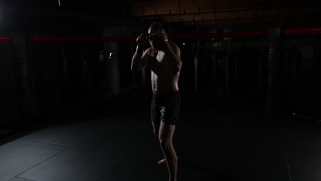 slow motion of a mma fighter, covered in sweat, in a ring, standing still in the guard position, the camera goes around, in a dark room, with a single light