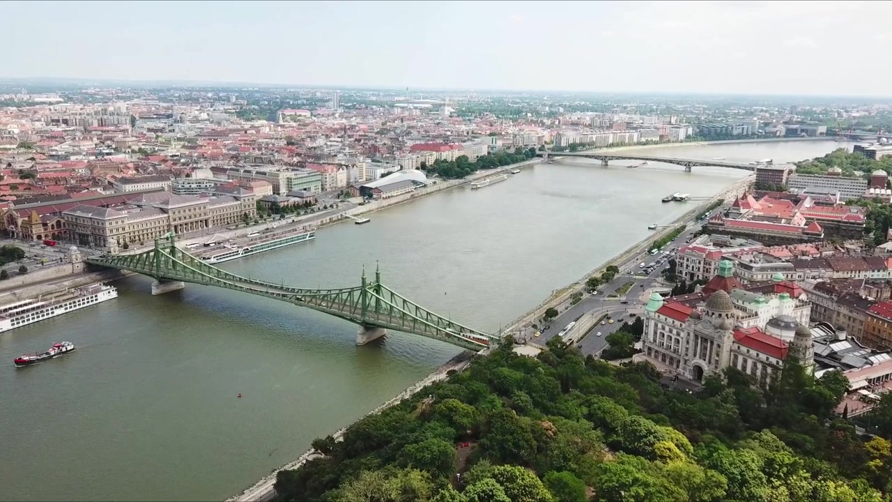 Ponte della Libertà, un ponte in acciaio verde che attraversa il fiume Danubio, collegando Buda e Pest a Budapest, Ungheria, mostrando il paesaggio urbano e il traffico fluviale in una giornata di sole, discesa di un drone al rallentatore.