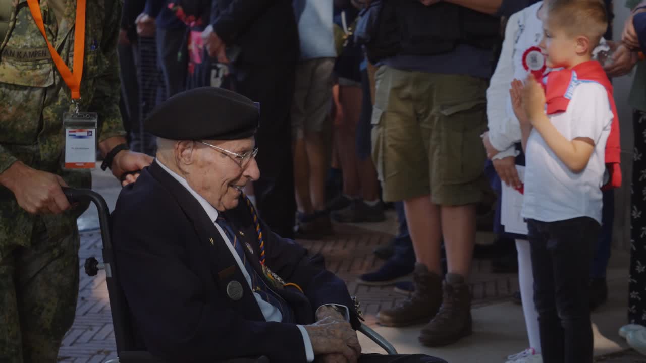 Elderly veteran is pushed in a wheelchair by a uniformed soldier during a military commemoration event. The solemn occasion pays tribute to the service and sacrifice of veterans