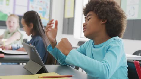 video of frustrated african american schoolboy sitting at desk using tablet in class, copy space