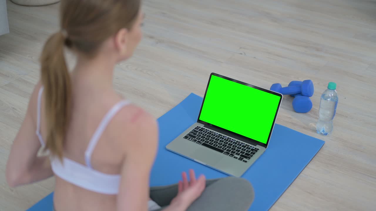 vista trasera de una mujer joven haciendo yoga mientras mira una computadora portátil con pantalla de tecla cromada