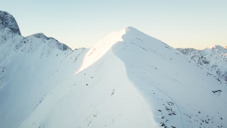 drone ascends sunlit slope to mountain summit, revealing majestic snowy peaks behind. filmed in andorra.