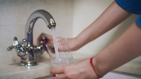 Woman-hand-turning-knob-on-faucet-and-pouring-water-into-glass