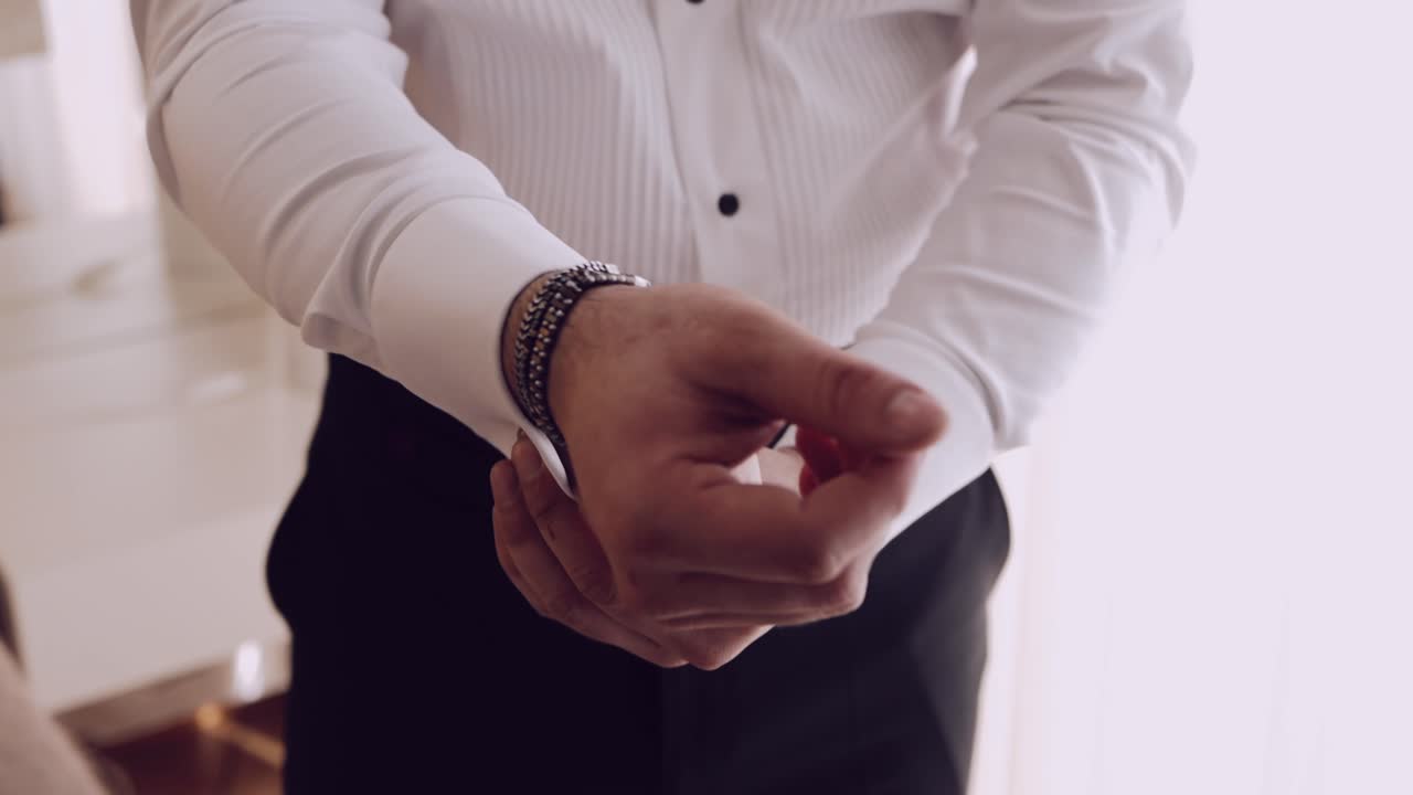 Close up of a man in an elegant white dress shirt adjusting his cufflinks