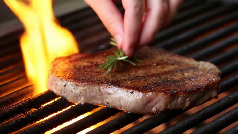 hand placing rosemary on a sizzling steak on a hot grill