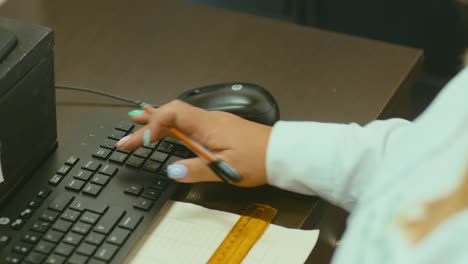 woman typing on a keyboard and operating a mouse on a wooden desk in an office