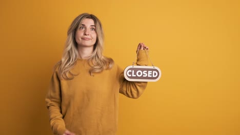 cheerful young woman showing closed signboard in hand on yellow background