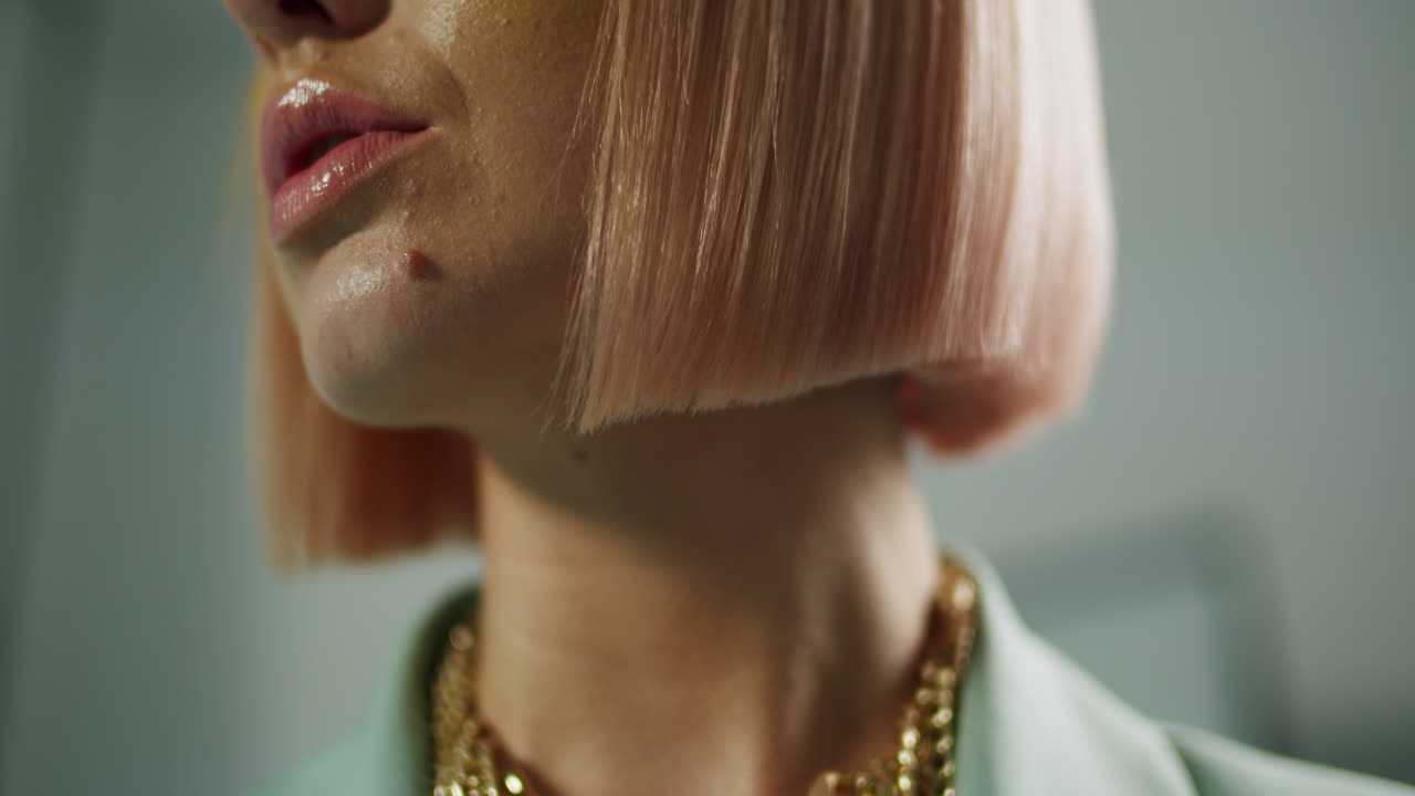 Primo piano di una donna alla moda con un caschetto rosa e una collana d'oro che gira la testa
