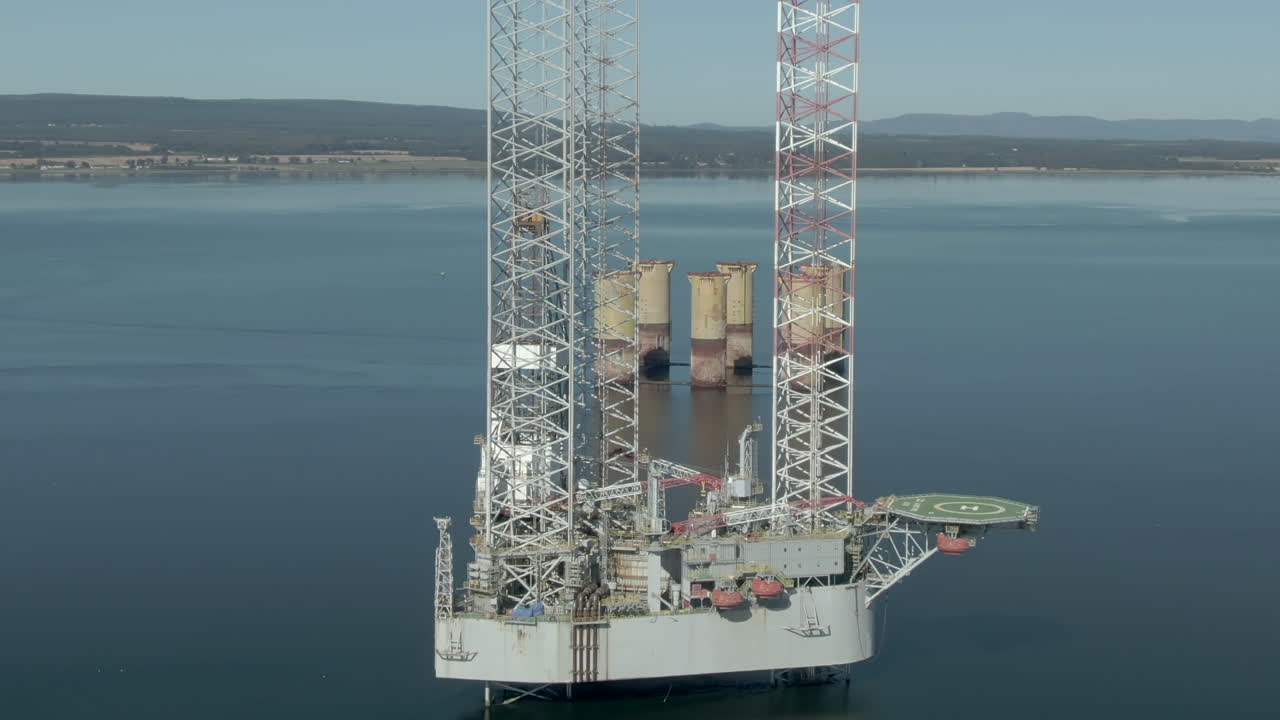 An aerial view of an oil rig on the Cromarty Firth on a sunny summer's day. Rotating clockwise around the rig with zoom in.