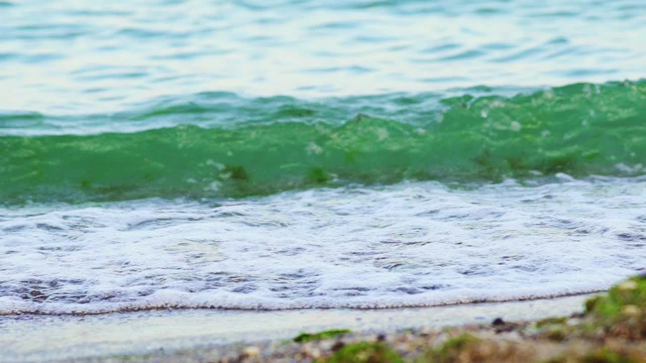 Water's waves dancing at the edge of the sea on a beach. White waves of transparent water on paradise beach in summer. Slow motion. Cose-up