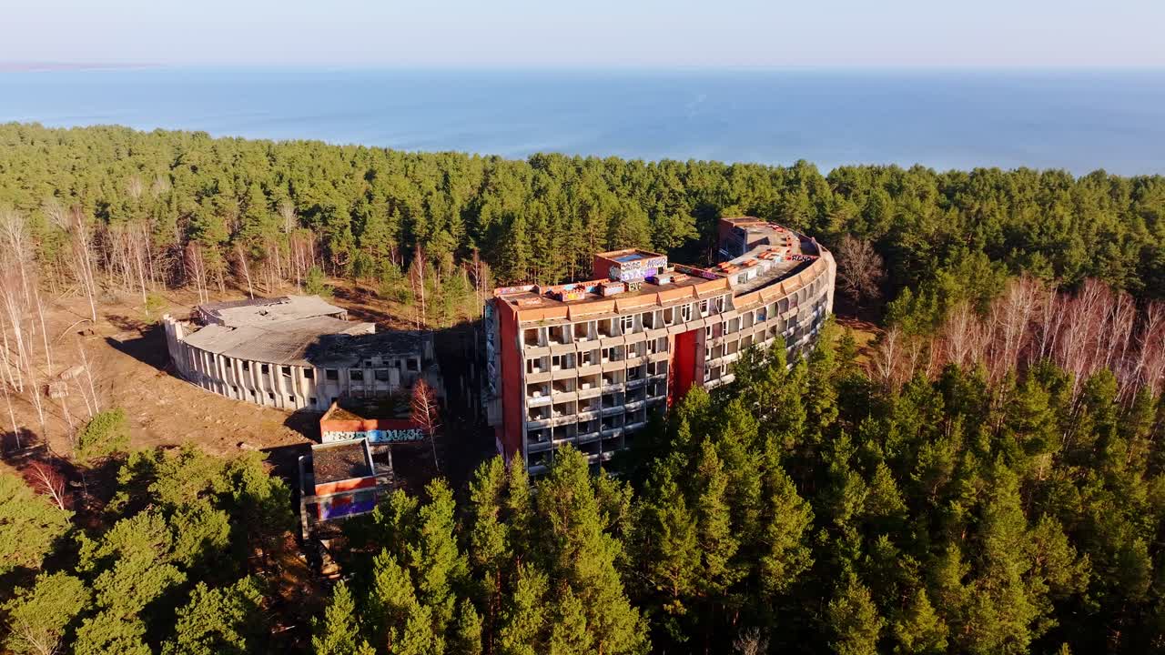 Old hotel ruin stands in pine forest near Baltic Sea shoreline, soft spring sun
