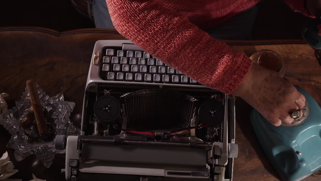 Novelist with whiskey and cigar calls on phone then loads typewriter to write
