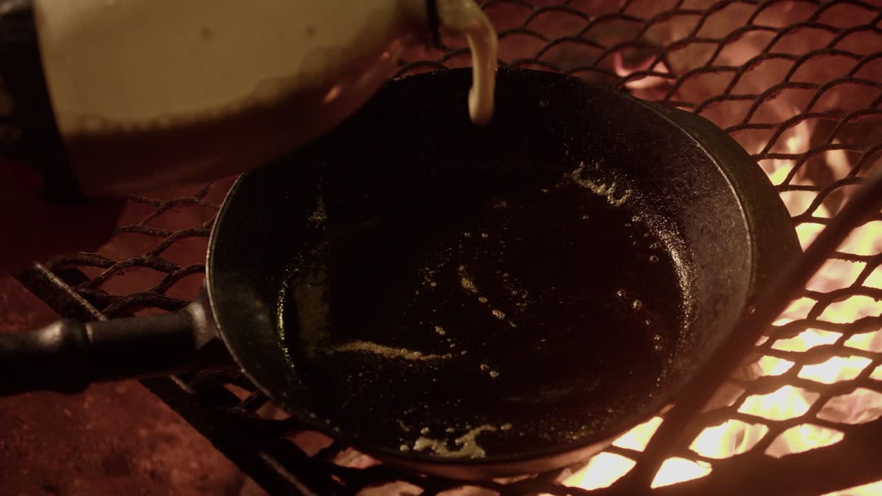 Lettutaikina kaadetaan kuumaan pannuun nuotiogrillillä yöllä.