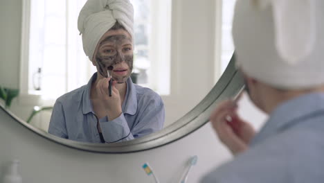 woman applying facial mask looking to the mirror 1