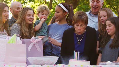 senior woman blows out candles at her birthday garden party