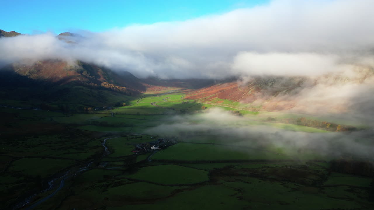 un valle verde sombreado rodeado de nubes, montañas envueltas iluminadas por la luz del sol de otoño de la mañana temprano.