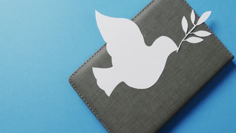 close up of white dove with leaf on grey notebook and copy space on blue background