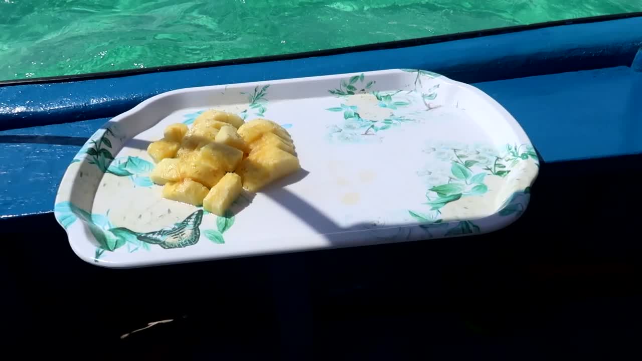 primer plano de piña en un plato en un barco de fibra azul navegando en las aguas turquesas del océano índico