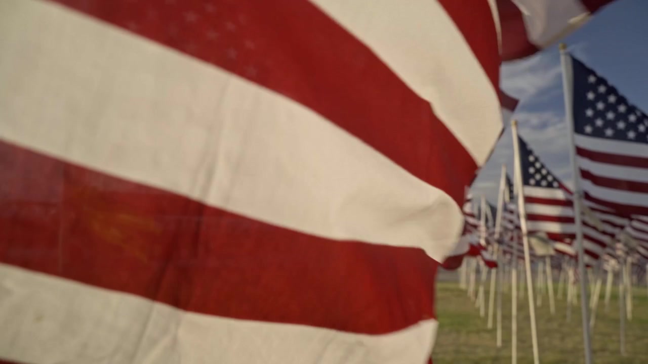 Ekstremt nærbillede af et amerikansk flag, der blafrer i vinden ved solnedgang. De røde og hvide stofstriber fylder billedet og skaber en patriotisk abstrakt baggrund og et overgangselement.