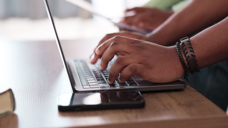 Laptop, Tastatur und tippende Männerhände beim Online-Arbeiten