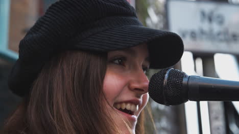 female musician busking playing acoustic guitar and singing outdoors in street