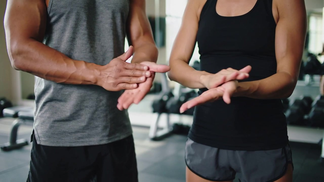 Sportpartners in tanktops wrijven hun handen, zich voorbereidend op een training in de gewichtenruimte bij halters.