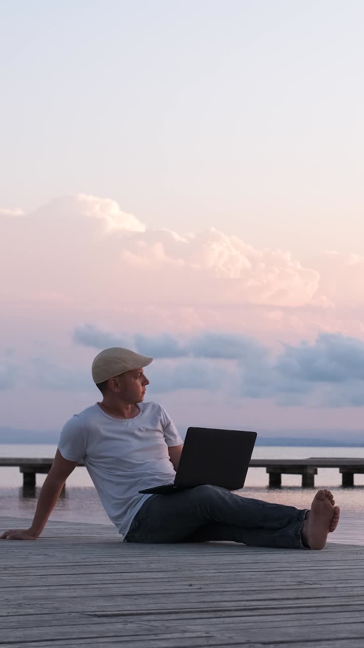 Male traveler sitting on the shore using laptop. Digital nomad or remote worker concept