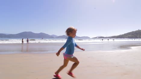 camera orbiting around young cute girl running freely on the beach with mountains background and calm sea and clear sand