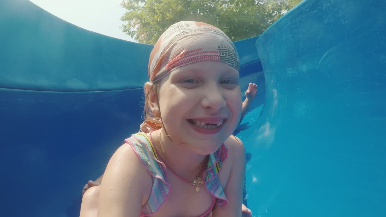 una familia feliz con un niño está montando un tobogán de agua riendo agitando sus manos a la cámara lenta m